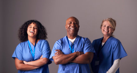 Studio Portrait Of Three Members Of Surgical Team Wearing Scrubs Standing Against Grey Background