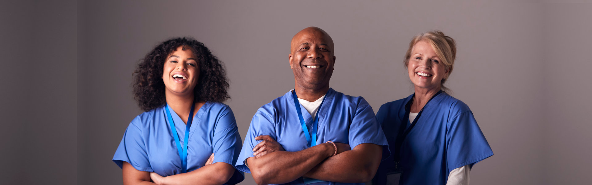 Studio Portrait Of Three Members Of Surgical Team Wearing Scrubs Standing Against Grey Background